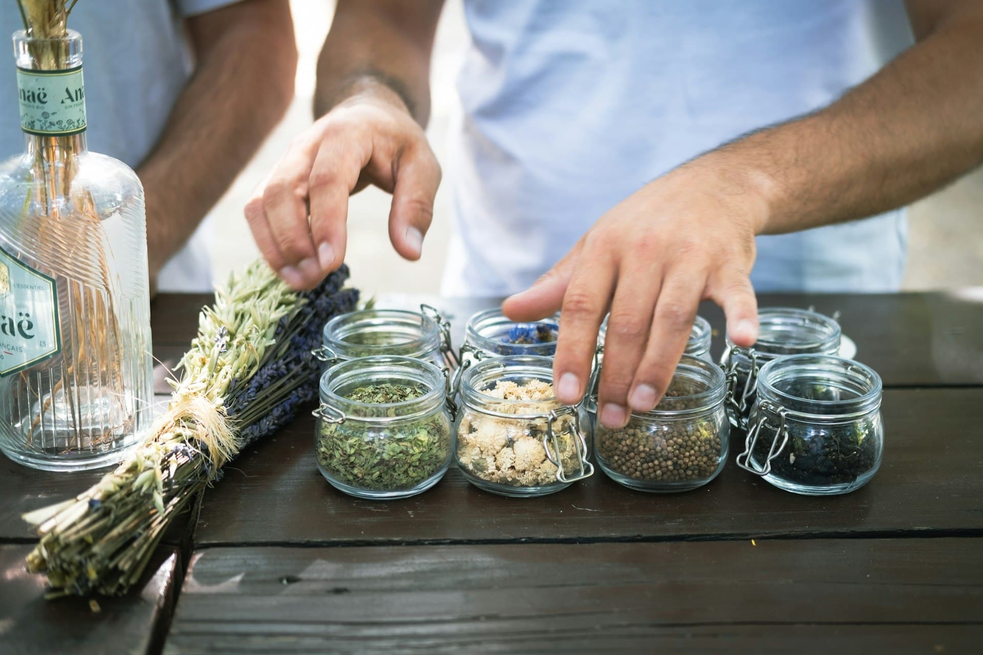 Hands arranging small glass jars of dried herbs and seeds on a wooden table