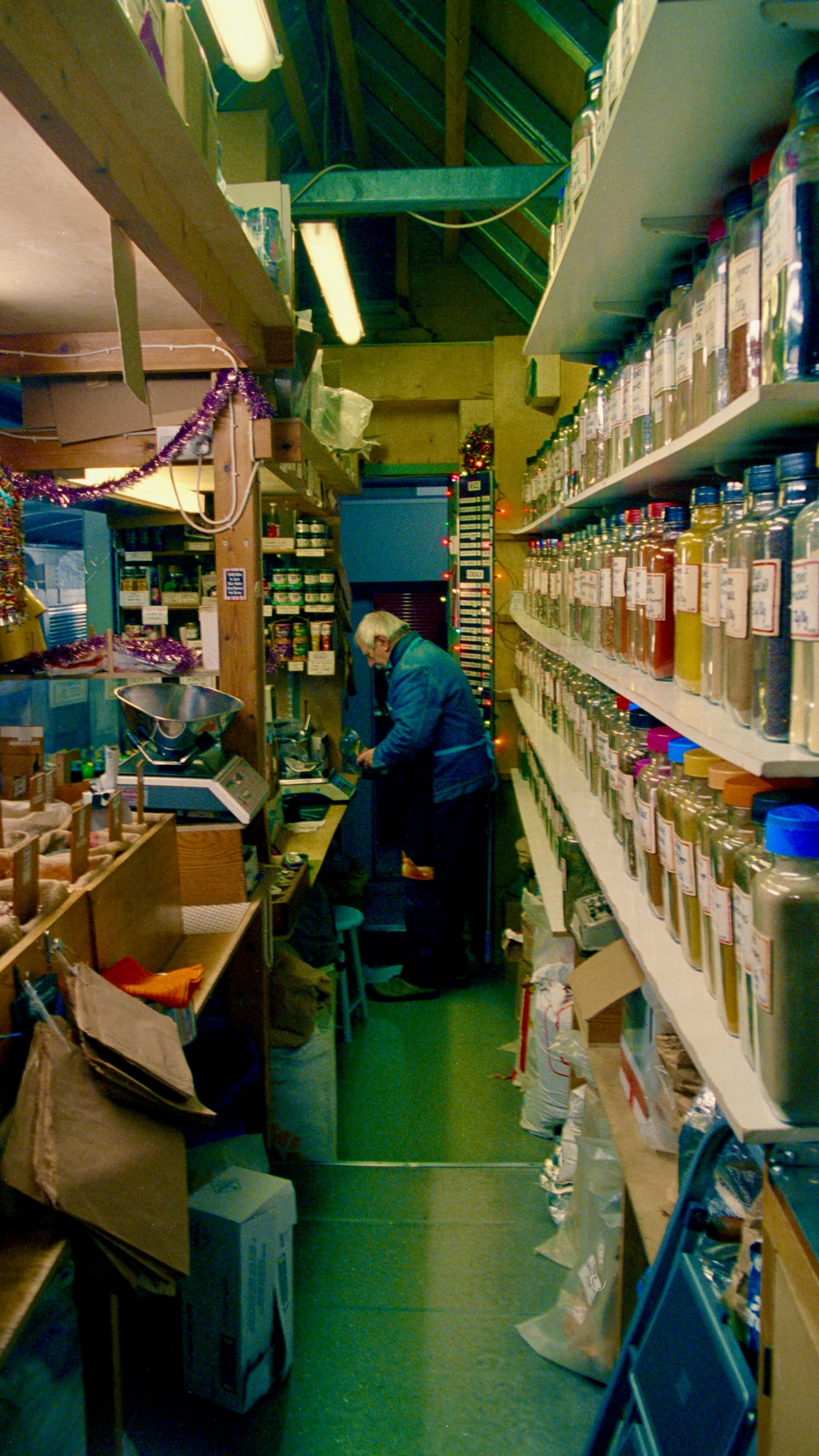 A shopkeeper at work in a narrow shop lined with shelves of spice jars
